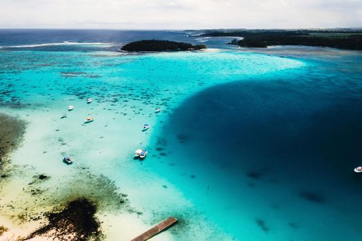 Aerial photography of the East coast of the island of Mauritius. the blue lagoon of the island of Mauritius is shot through from above. The boat is floating on a turquoise lagoon.