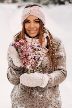 A girl in a sweater in winter with a bouquet in her hands stands among large snowdrifts.