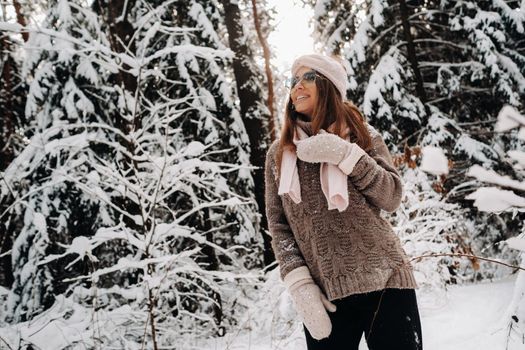 A girl in a sweater and glasses in winter in a snow-covered forest.