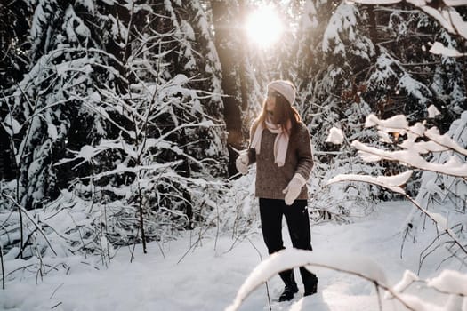 A girl in a sweater and glasses in winter in a snow-covered forest.