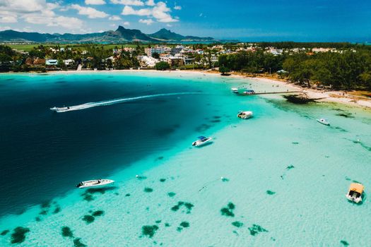 Aerial photography of the East coast of the island of Mauritius. the blue lagoon of the island of Mauritius is shot through from above. The boat is floating on a turquoise lagoon.