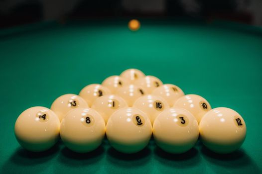 They play pool on a green table.The balls are placed in a triangle on the table