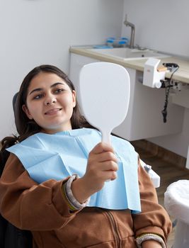 Young Woman Looking At Mirror With Smile In Dentist Office