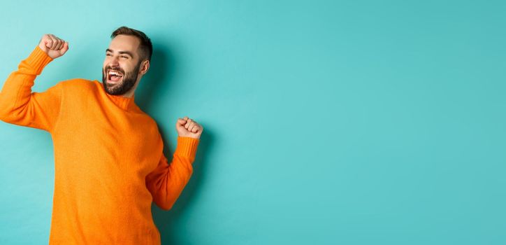 Happy man raising arm, feeling like winner, triumphing and celebrating, standing over light blue background.