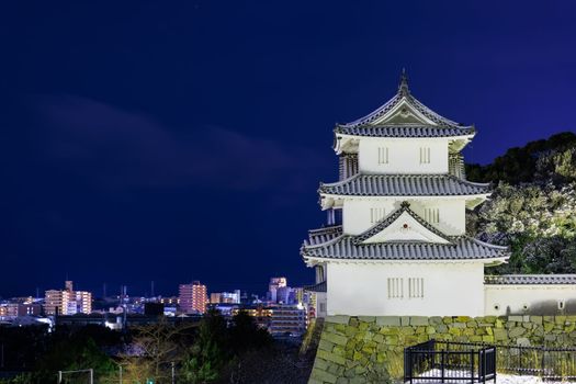 Historic Japanese castle lit at night with lights from modern city in background. High quality photo