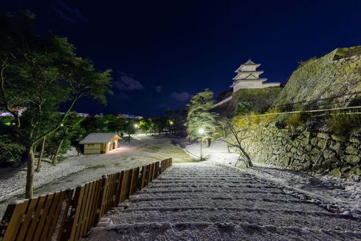 Snow covered stairs by stone wall and castle tower in deserted park on cold winter night. High quality photo