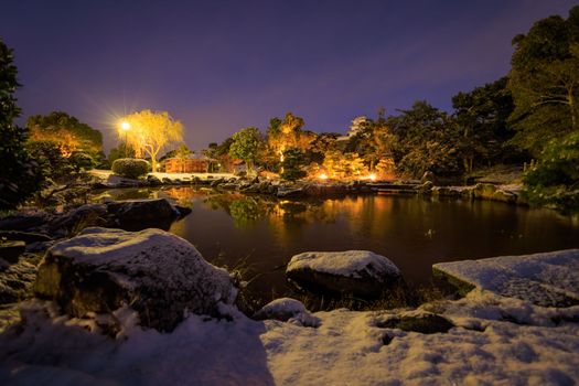 Snow on small pond in Japanese garden with lights on cold winter night. High quality photo