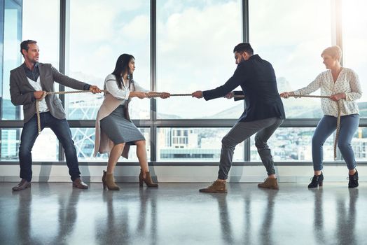 The business world is quite a competitive one. a group of businesspeople pulling on a rope during tug of war in an office
