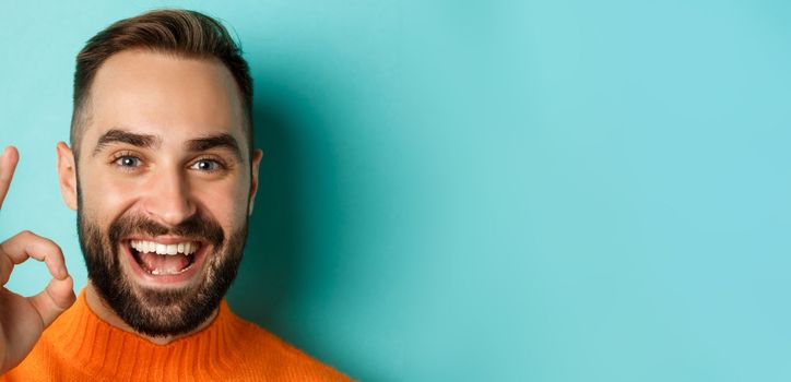 Close-up of confident and happy man with beard showing okay sign, approve and like, giving positive reply or agree, standing over turquoise background.