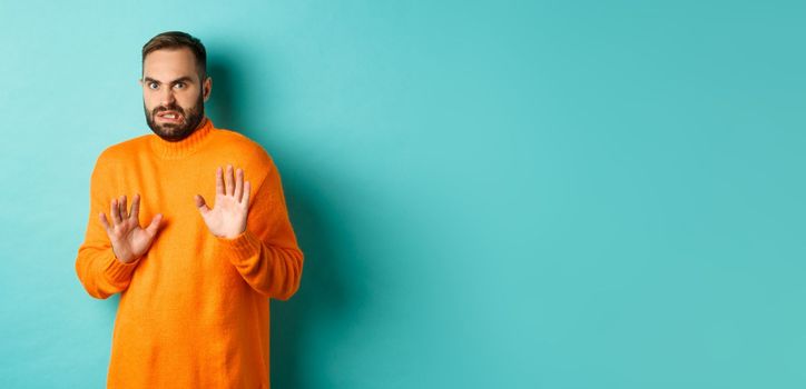 Alarmed guy shaking hands in rejection, declining and stepping away scared, standing over light blue background.