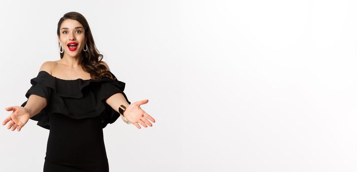 Fashion and beauty concept. Happy young woman in glamour black dress, reaching hands forward to take something, waiting for hug, white background.