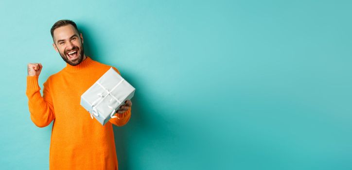 Holidays and celebration concept. Excited man receiving gift, looking happy at present and smiling, standing over blue background.