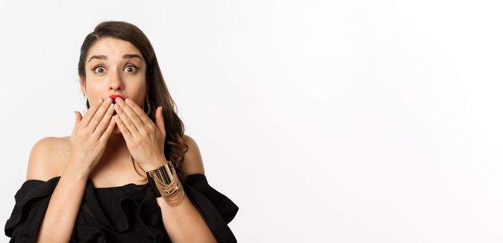 Fashion and beauty concept. Close-up of excited young woman looking amazed, cover mouth with hands and staring at camera with rejoice, white background.