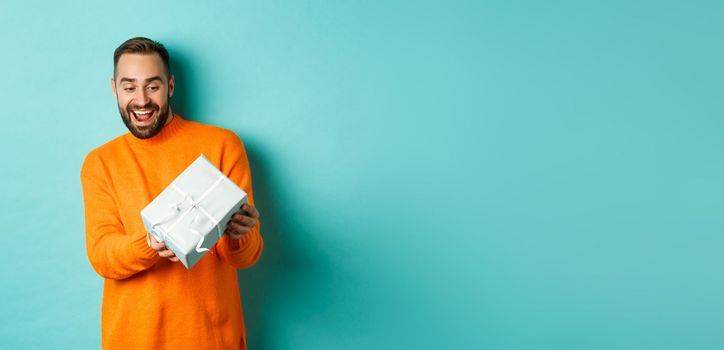 Holidays and celebration concept. Excited man receiving gift, looking happy at present and smiling, standing over blue background.