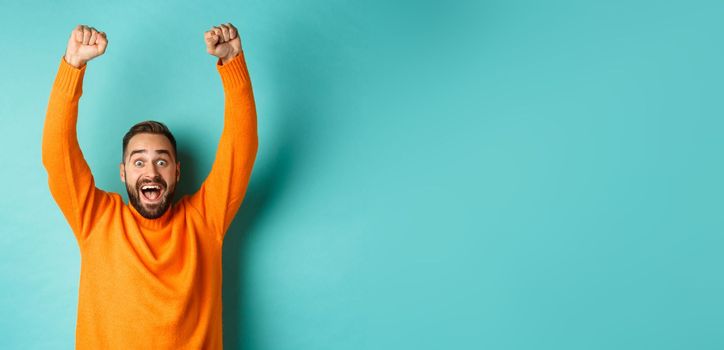 Waist-up shot of happy guy celebrating victory, rejoicing of winning a bet, achieve goal and smiling satisfied, shouting yes, standing over light blue background.