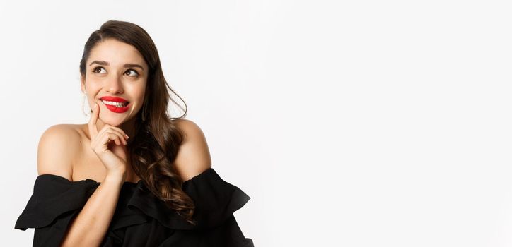 Fashion and beauty concept. Close-up of beautiful dreamy woman with red lips, looking at upper left corner and smiling tempted, having idea, standing over white background.