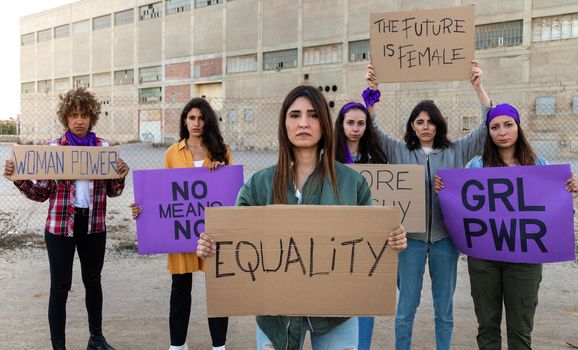 Confident group of multiracial women looking at camera holding feminist signboards protesting for women empowerment. Panoramic banner. Equality concept.