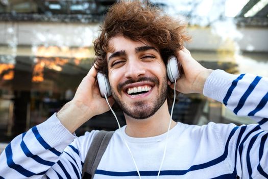 Happy young man relaxing outdoors listening to music using headphones looking at camera. Lifestyle concept.