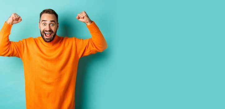 Handsome man celebrating victory, winning and looking happy, triumphing over win, standing over light blue background.