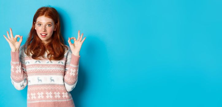 Image of young confident redhead woman showing okay signs, assure all good, praising choice, standing over blue background.