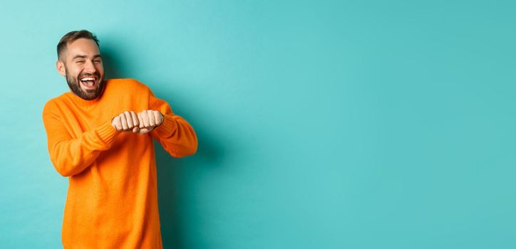 Happy man dancing and celebrating success, feeling like winner, smiling and rejoicing, light blue background.