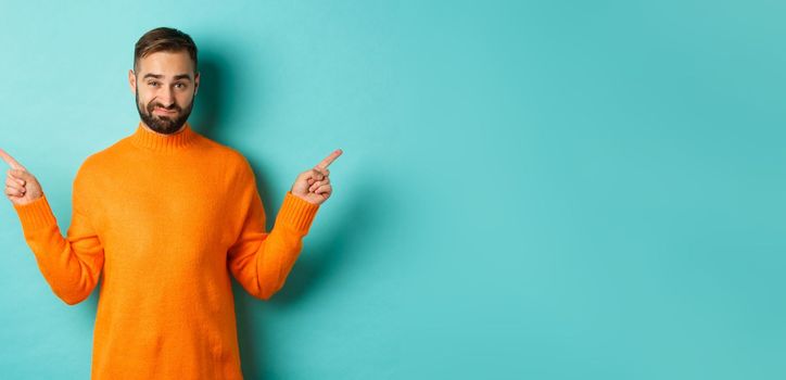 Doubtful and indecisive man pointing fingers sideways, showing different sides, two choices, looking skeptical, standing over light blue background.