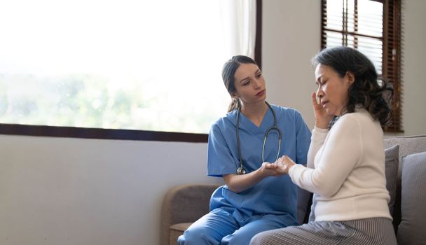 Young female physician leaning forward to elderly lady patient holding her hand in palms. supporting encouraging old person...