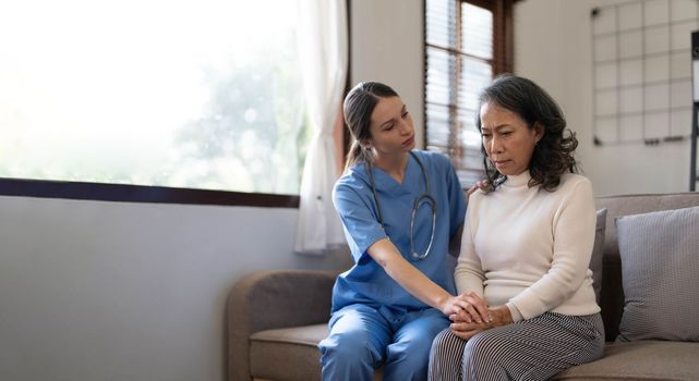 Young female physician leaning forward to elderly lady patient holding her hand in palms. supporting encouraging old person...