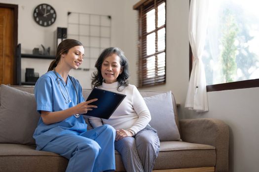 Asian nurse showing health checkup report to grandmather and giving advice. medical assisted living visit senior patient at home. Home nursing and healthcare caregiver concept..