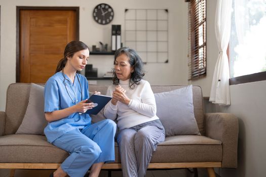 Asian nurse showing health checkup report to grandmather and giving advice. medical assisted living visit senior patient at home. Home nursing and healthcare caregiver concept..