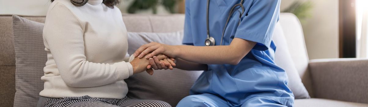 Happy patient is holding caregiver for a hand while spending time together. Elderly woman in nursing home and nurse...