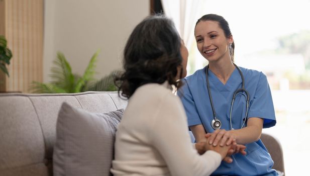 Happy patient is holding caregiver for a hand while spending time together. Elderly woman in nursing home and nurse...