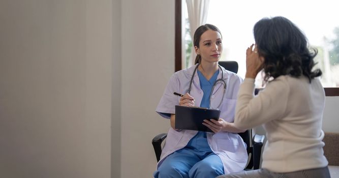 Asian female patient undergoing health check up while female doctor uses stethoscope to check heart rate in nurse, health care concept..