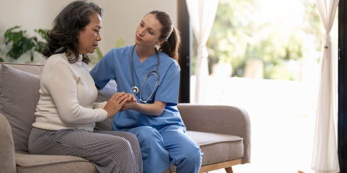 Happy patient is holding caregiver for a hand while spending time together. Elderly woman in nursing home and nurse...