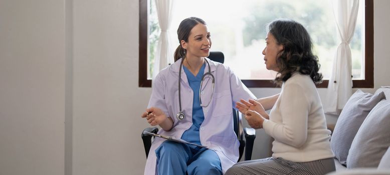 Asian female patient undergoing health check up while female doctor uses stethoscope to check heart rate in nurse, health care concept..