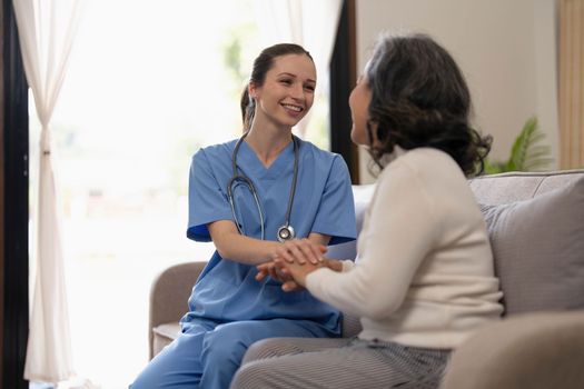 Happy patient is holding caregiver for a hand while spending time together. Elderly woman in nursing home and nurse...