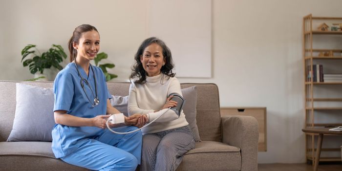 Happy senior woman having her blood pressure measured in a nursing home by her caregiver. Happy nurse measuring blood pressure of a senior woman in living room..