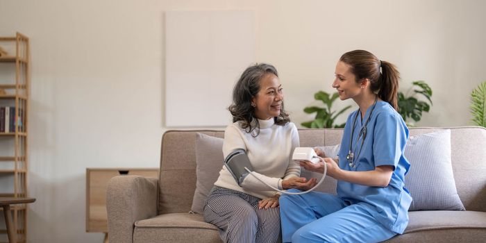 Happy senior woman having her blood pressure measured in a nursing home by her caregiver. Happy nurse measuring blood pressure of a senior woman in living room..