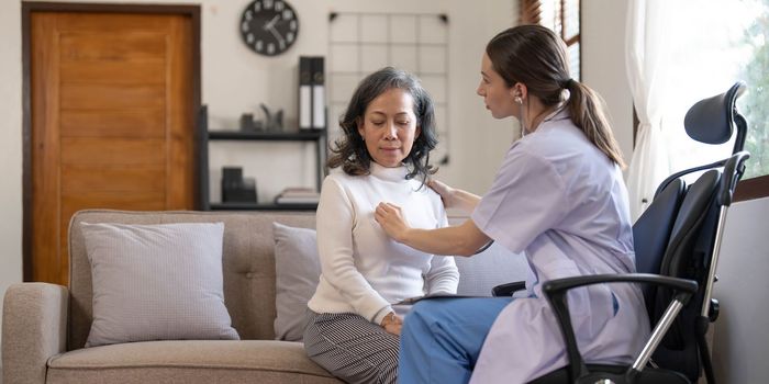 Asian female patient undergoing health check up while female doctor uses stethoscope to check heart rate in nurse, health care concept..