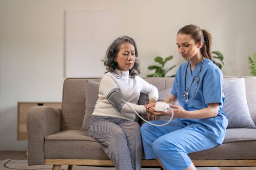 Happy senior woman having her blood pressure measured in a nursing home by her caregiver. Happy nurse measuring blood pressure of a senior woman in living room..