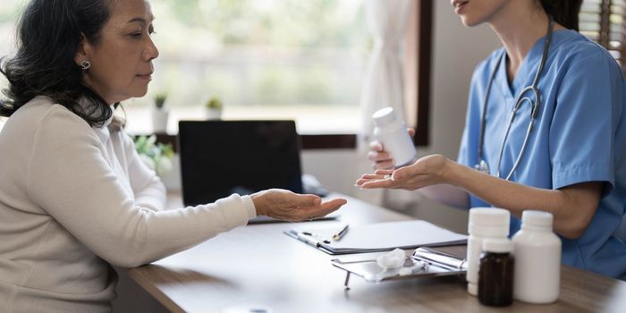 Asian Female Doctor examining and taking note on checklist paper with female patients in medical room...