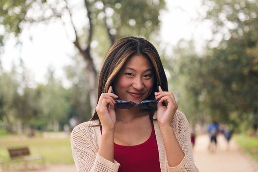 young asian woman looking at camera with mischief taking of her sunglasses, concept of youth and beauty
