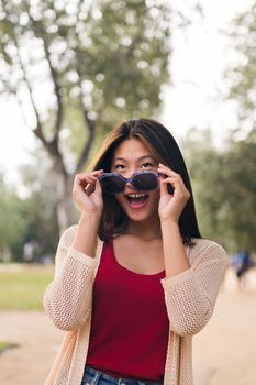 vertical portrait of a cheerful asian woman looking happy over her sunglasses, concept of youth and beauty