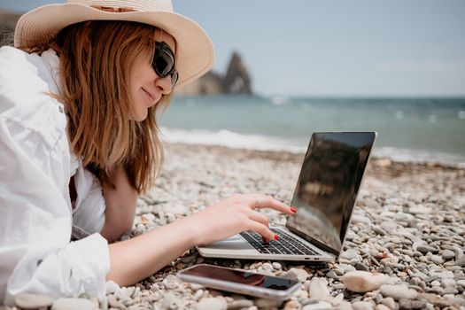 Woman sea laptop. Business woman in yellow hat working on laptop by sea. Close up on hands of pretty lady typing on computer outdoors summer day. Freelance, digital nomad, travel and holidays concept