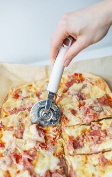 Juicy delicious slice of pizza with ham, onion and cheese. The chef cuts the pizza into pieces with a knife. Cooking pizza at home