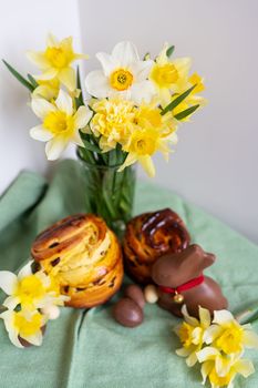 Homemade Easter traditional pastries lie on a green napkin along with daffodil flowers, rabbit, chocolate eggs. Easter baking and decor, vertical photo