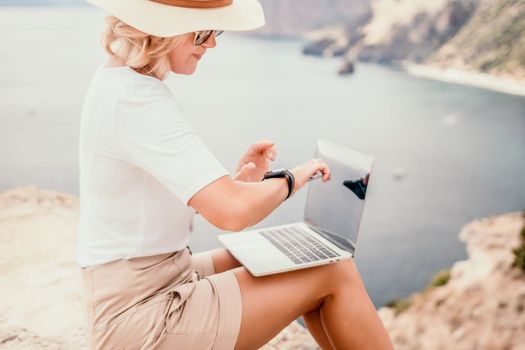 Digital nomad, Business woman working on laptop by the sea. Pretty lady typing on computer by the sea at sunset, makes a business transaction online from a distance. Freelance remote work on vacation