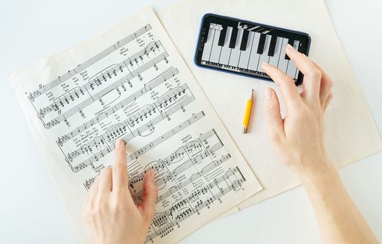 Lviv, Ukraine - December 13, 2022: The program on the phone to play the piano, piano score. Musical notes on paper. The program on the smartphone, practice. View from above