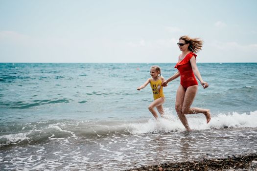 Happy loving family mother and daughter having fun together on the beach. Mum playing with her kid in holiday vacation next to the ocean - Family lifestyle and love concept.