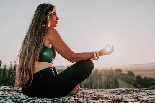 Well looking middle aged woman with long hair, fitness instructor in leggings and tops doing stretching and pilates on the rock near forest. Female fitness yoga routine concept. Healthy lifestyle.